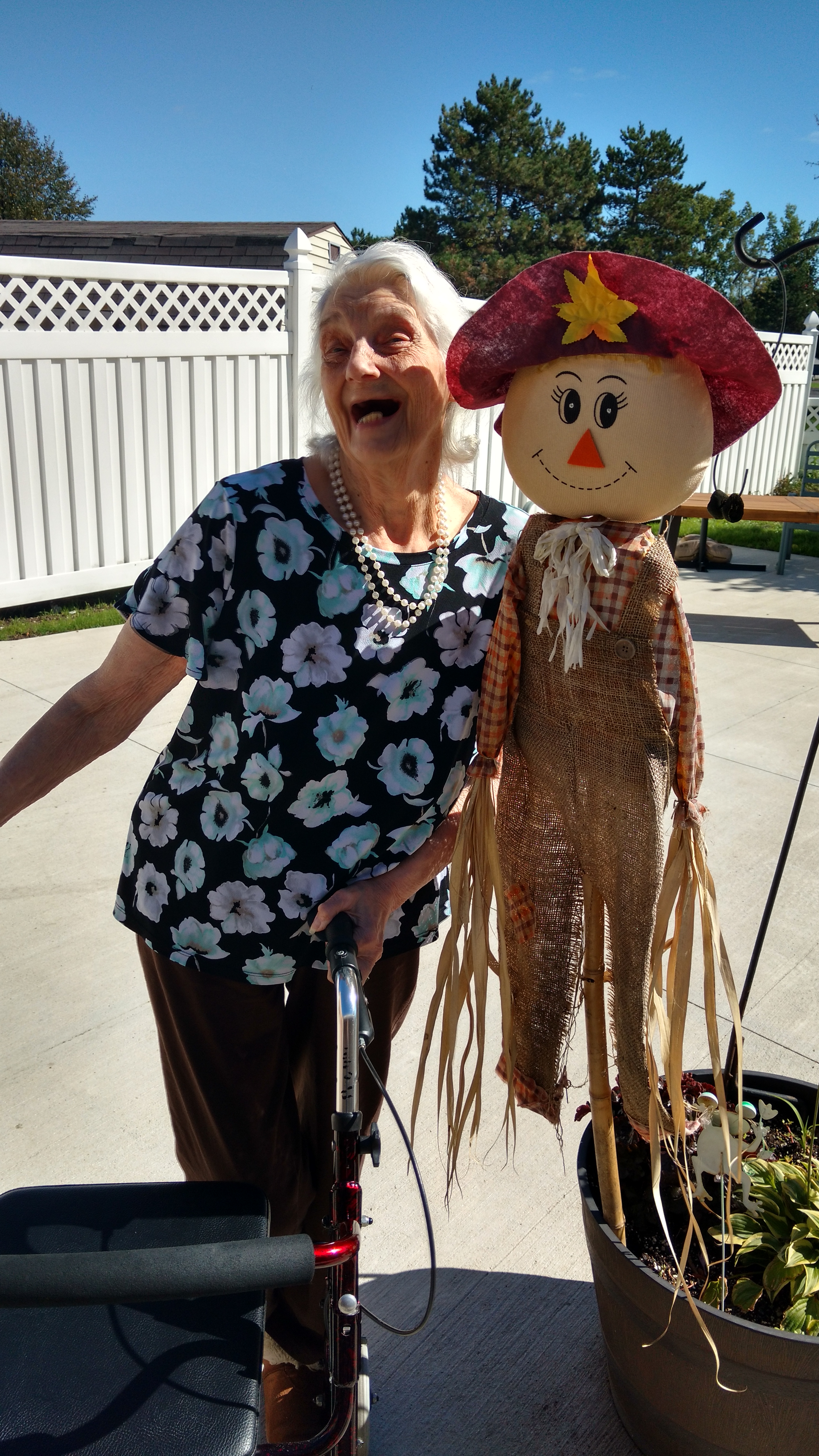 resident smiling next to a scarecrow decoration